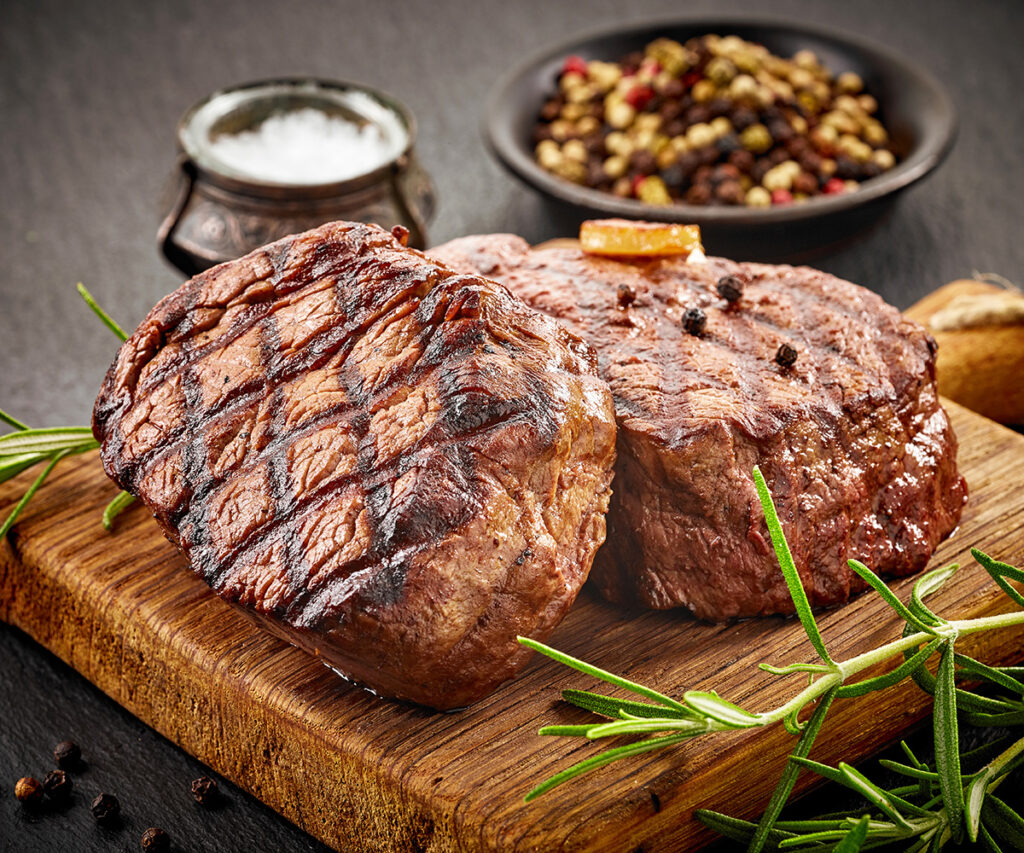 Steaks on wooden serving plate.